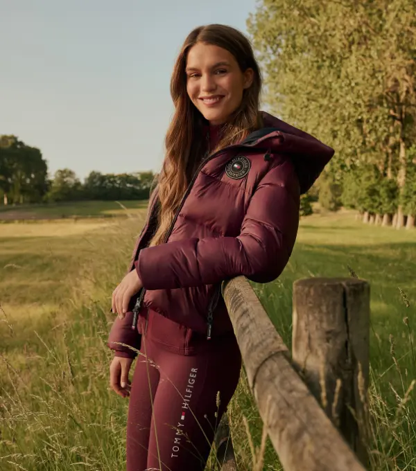 Woman in a burgundy riding jacket at a pasture fence